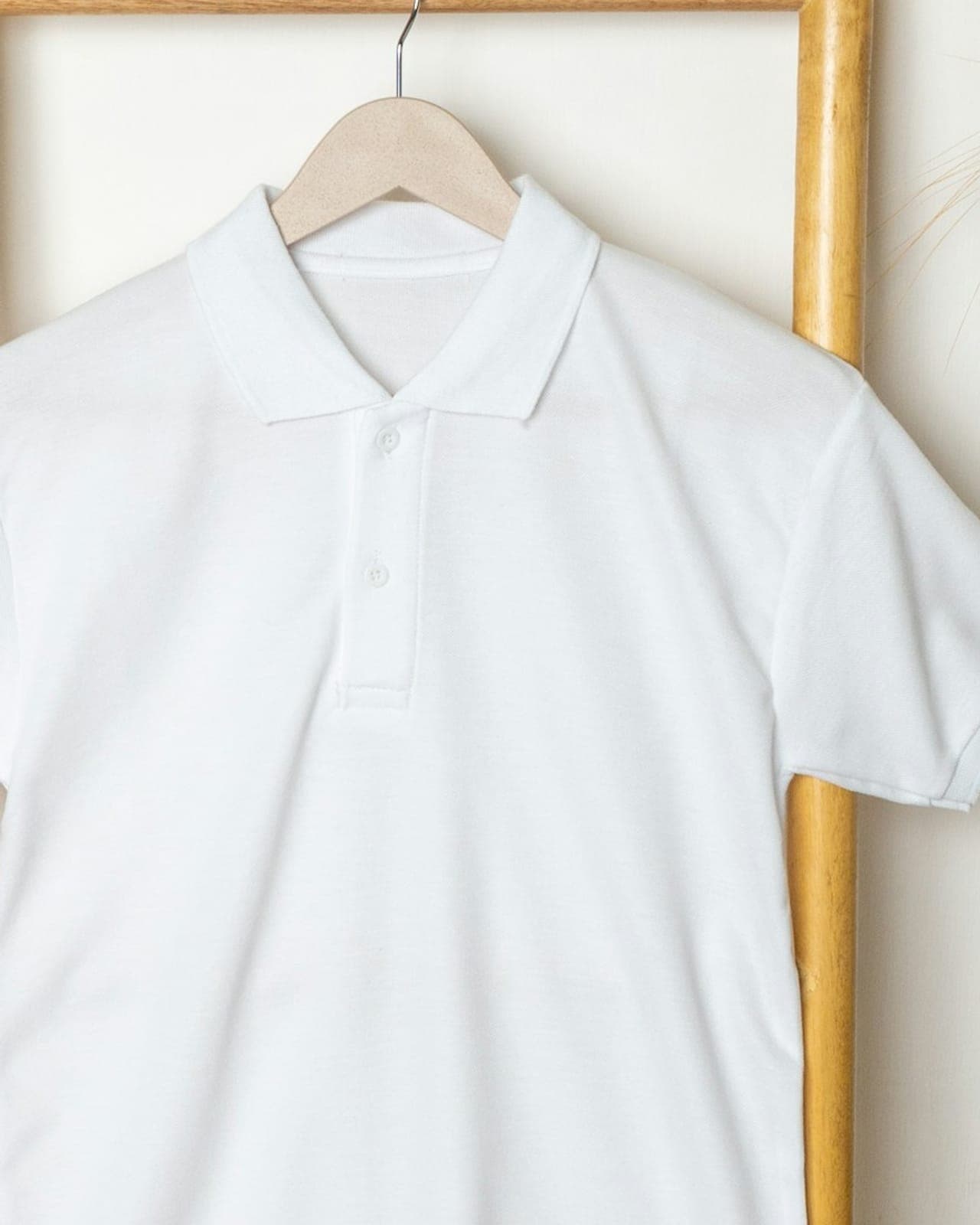 White piqué polo shirt on a wooden hanger, showing the knitted collar and buttoned placket