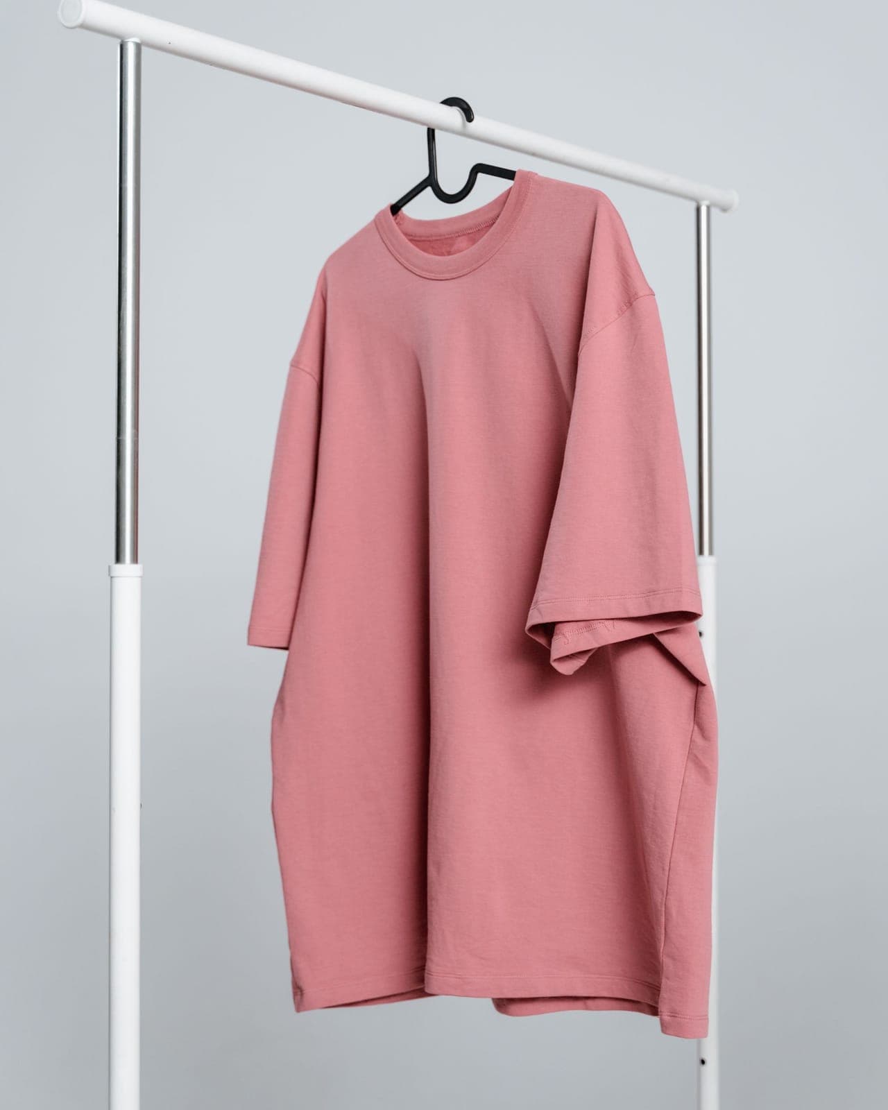 Oversized pink crewneck sweatshirt hanging on a clothing rail against a plain background