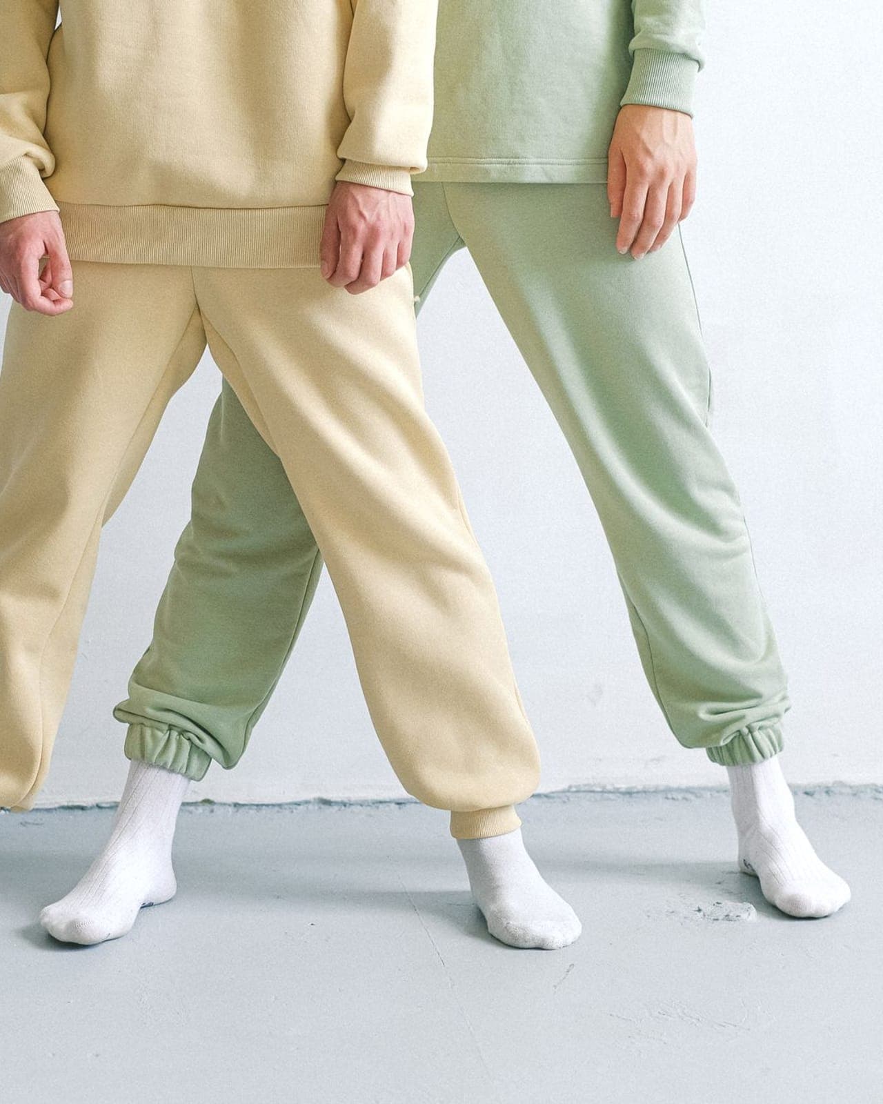 Two coordinated tracksuits in pale yellow and sage green, each with matching top and joggers